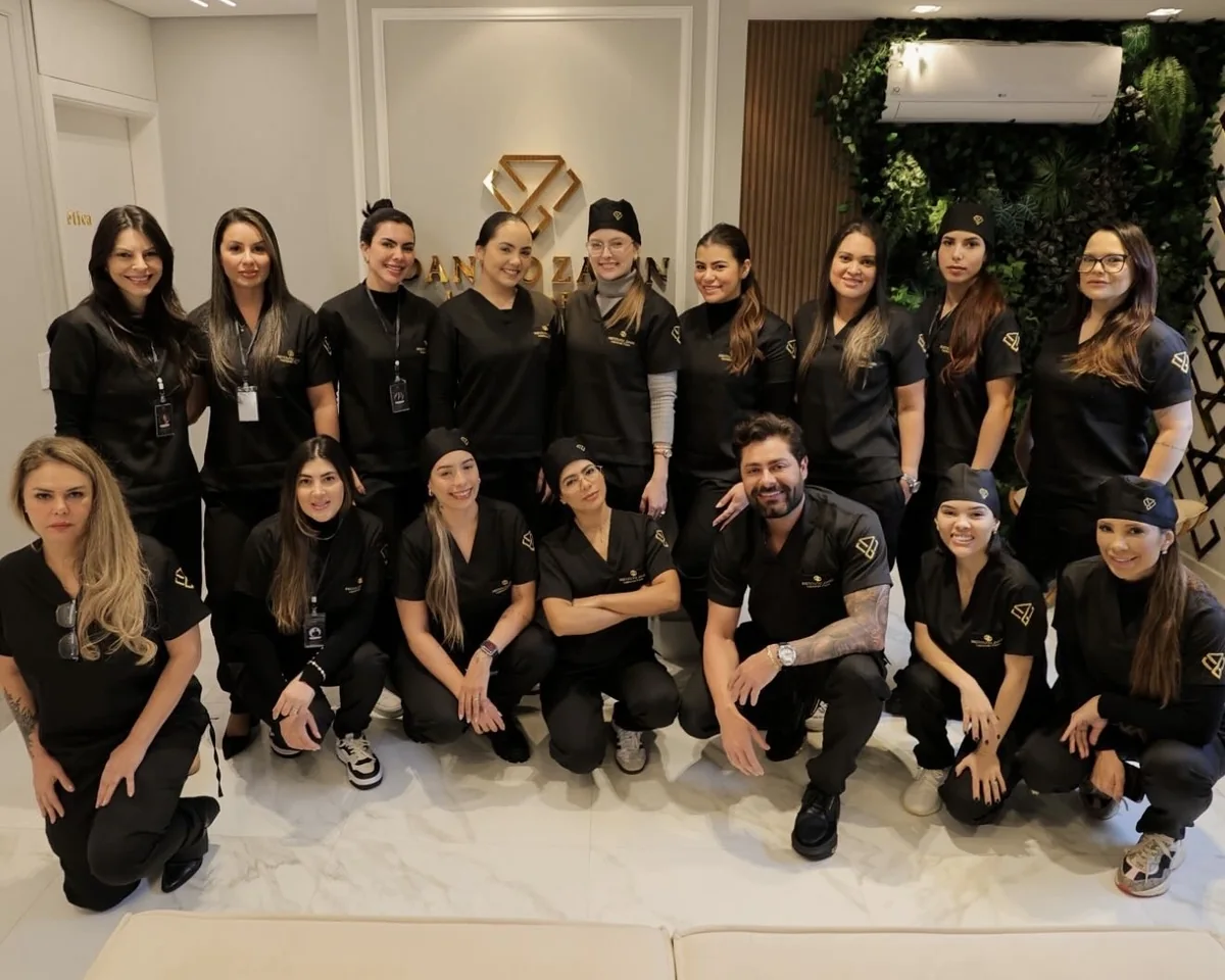 Dr. Danilo Zanin com a turma do curso Lapidando Faces, todos de uniforme preto, em frente ao logo do instituto