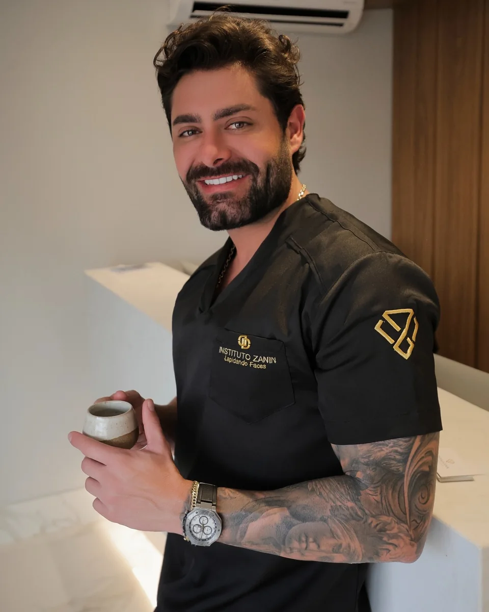 Dr. Danilo Zanin sorrindo, com o uniforme preto do Instituto Zanin e uma xícara de café na mão