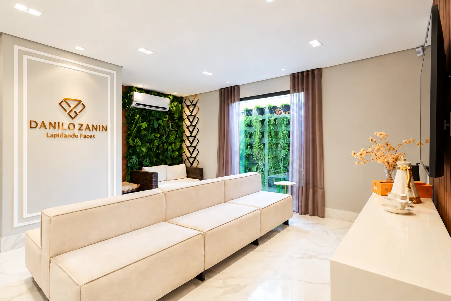 Sala de espera do instituto, com sofá claro, jardim vertical e o logo Danilo Zanin na parede